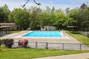 A swimming pool with a fenced area, a small building, and trees in the background.