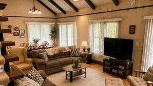 Ein gemütliches Wohnzimmer mit einer Couch, Sesseln, einem Couchtisch, einem Fernseher und einem Bücherregal.
