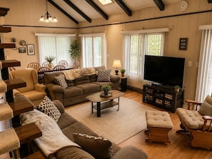 A cozy living room with a sofa, armchairs, a coffee table, a TV, and a bookshelf.