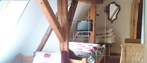 Un dormitorio acogedor en el ático con una cama de madera, un escritorio pequeño, una silla y un televisor.