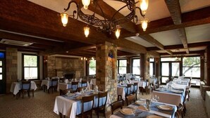 A restaurant with multiple tables set for dining, stone pillars, and a chandelier. - Calidus Hotel (Ayvacik)