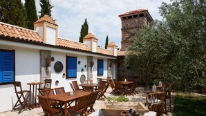 An outdoor patio with wooden tables and chairs, stone flooring, and a stone wall with a chimney. - Calidus Hotel (Ayvacik)