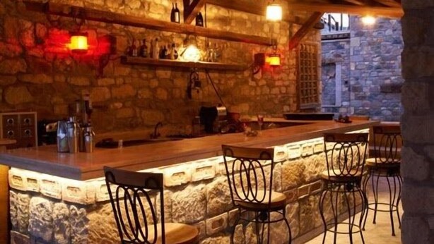 A rustic bar area with stone walls, wooden beams, and metal bar stools. - Calidus Hotel (Ayvacik)