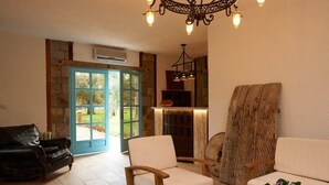 A spacious living area with a stone wall, a wooden chair, a black leather sofa, and a wooden coffee table. - Calidus Hotel (Ayvacik)