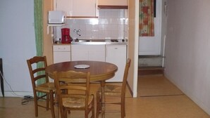 Una cocina compacta con gabinetes blancos, una cafetera roja y una mesa de comedor con sillas.