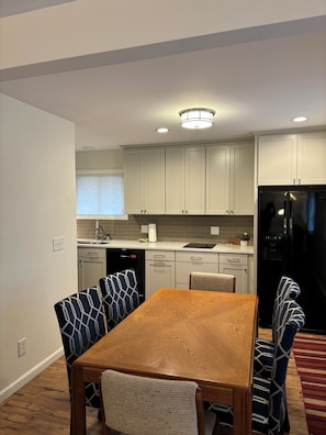 A modern kitchen with white cabinets, a black refrigerator, and a wooden dining table with patterned chairs.