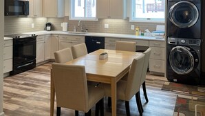 A modern kitchen with white cabinets, a dining table with chairs, a built-in oven, a microwave, a dishwasher, and a stacked washer and dryer. - Beautiful Mountain Getaway in Breckenridge, CO (Breckenridge)