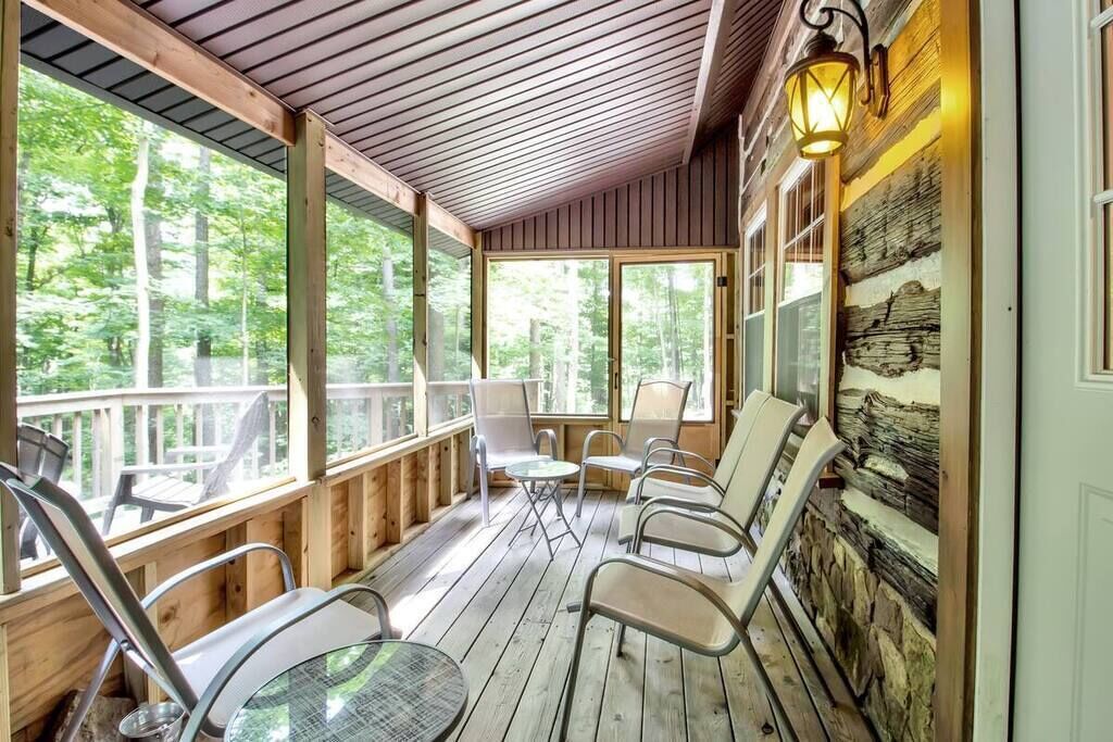 Une terrasse en bois avec des chaises et une table, de grandes fenêtres et une lanterne.