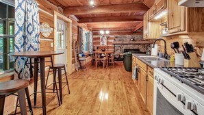 A wooden cabin interior with a kitchen, dining area, and bar. - Cherry Grove - Rustic Log Cabin (Cherry Creek)