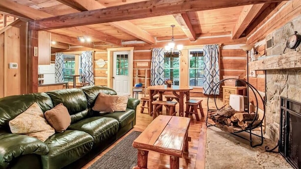 A cozy log cabin interior with a green leather sofa, wooden dining table, and a fireplace. - Cherry Grove - Rustic Log Cabin (Cherry Creek)