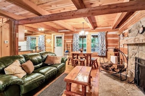 L’intérieur chaleureux d’un chalet en rondins, avec un canapé en cuir vert, une table à manger en bois et une cheminée.