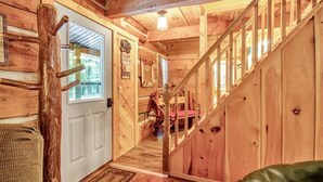 A wooden cabin interior with a staircase leading to a second floor, a door with a window, and a visible bathroom area. - Cherry Grove - Rustic Log Cabin (Cherry Creek)