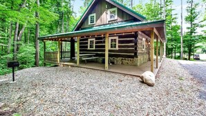 A log cabin with a covered porch and picnic tables, surrounded by a forest. - Cherry Grove - Rustic Log Cabin (Cherry Creek)