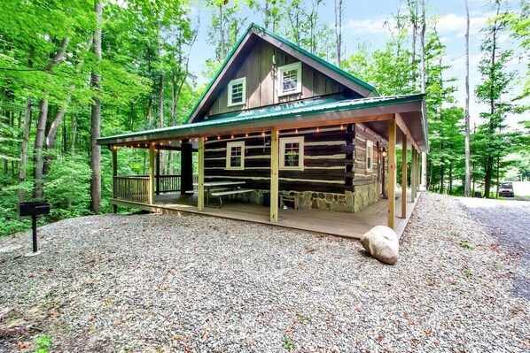 Une cabane en rondins dotée d’un porche couvert et de tables de pique-nique, entourée d’une forêt.