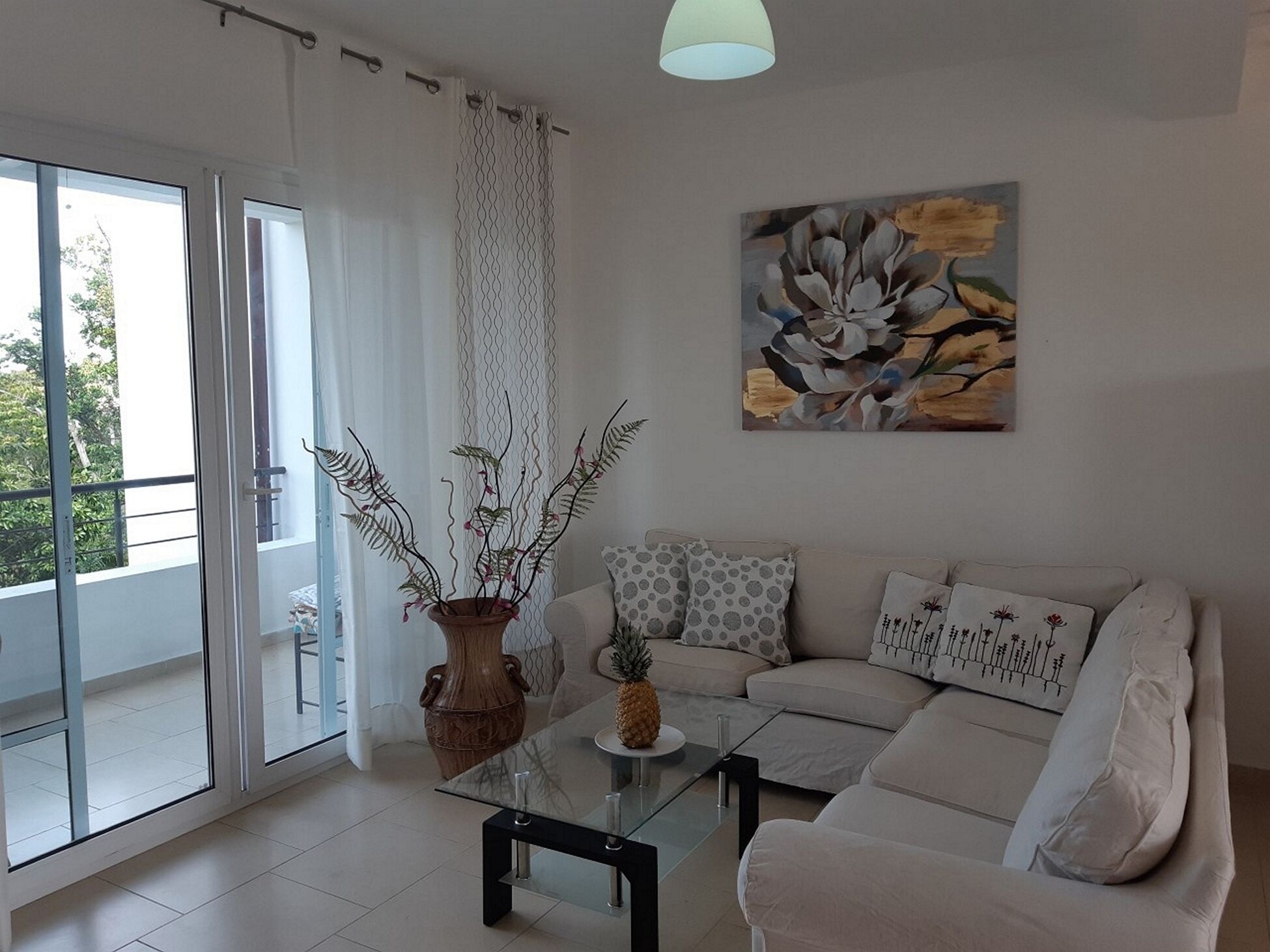 A modern living room with a glass coffee table, a beige sofa, and a large window with a view of greenery.