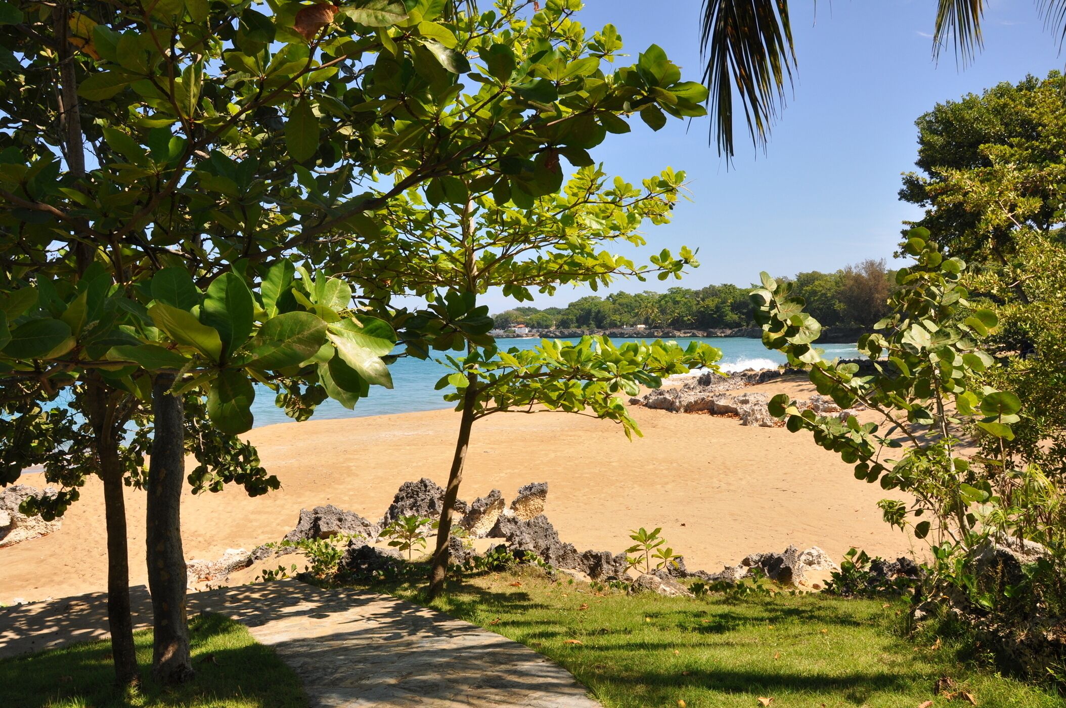 A beach with a clear view of the sea, surrounded by greenery and rocks.