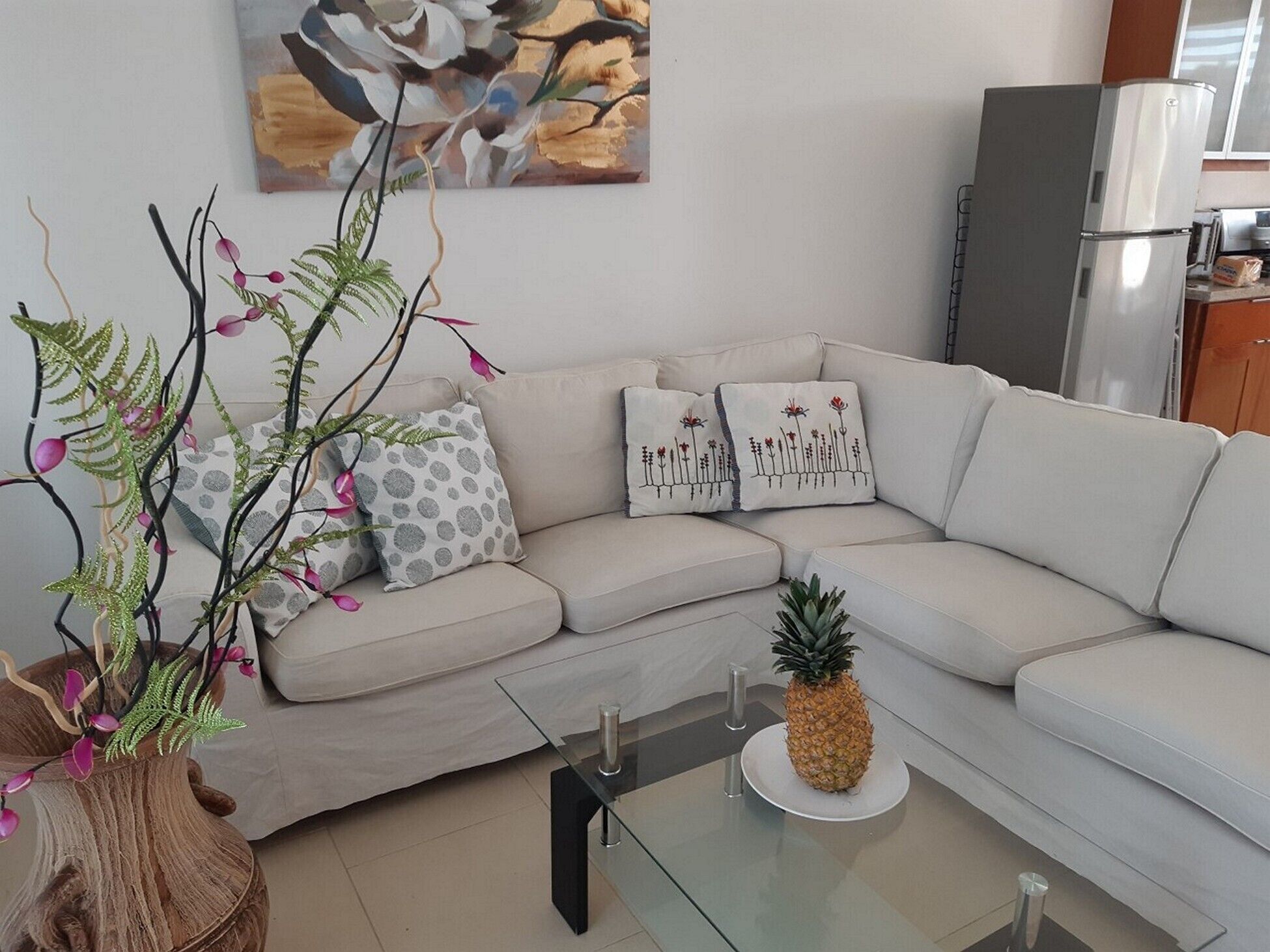 Een moderne woonkamer met een beige bank, decoratieve kussens, een glazen salontafel en een ananas als decoratie.