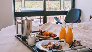 A breakfast tray with coffee, toast, eggs, and juice on a bed with a view of a balcony and a chair. - Geneseo Inn (Paso Robles)