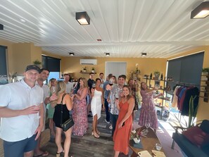 A group of people in a room with a high ceiling, a visible air conditioning unit, and a clothing rack with various garments. - Geneseo Inn (Paso Robles)
