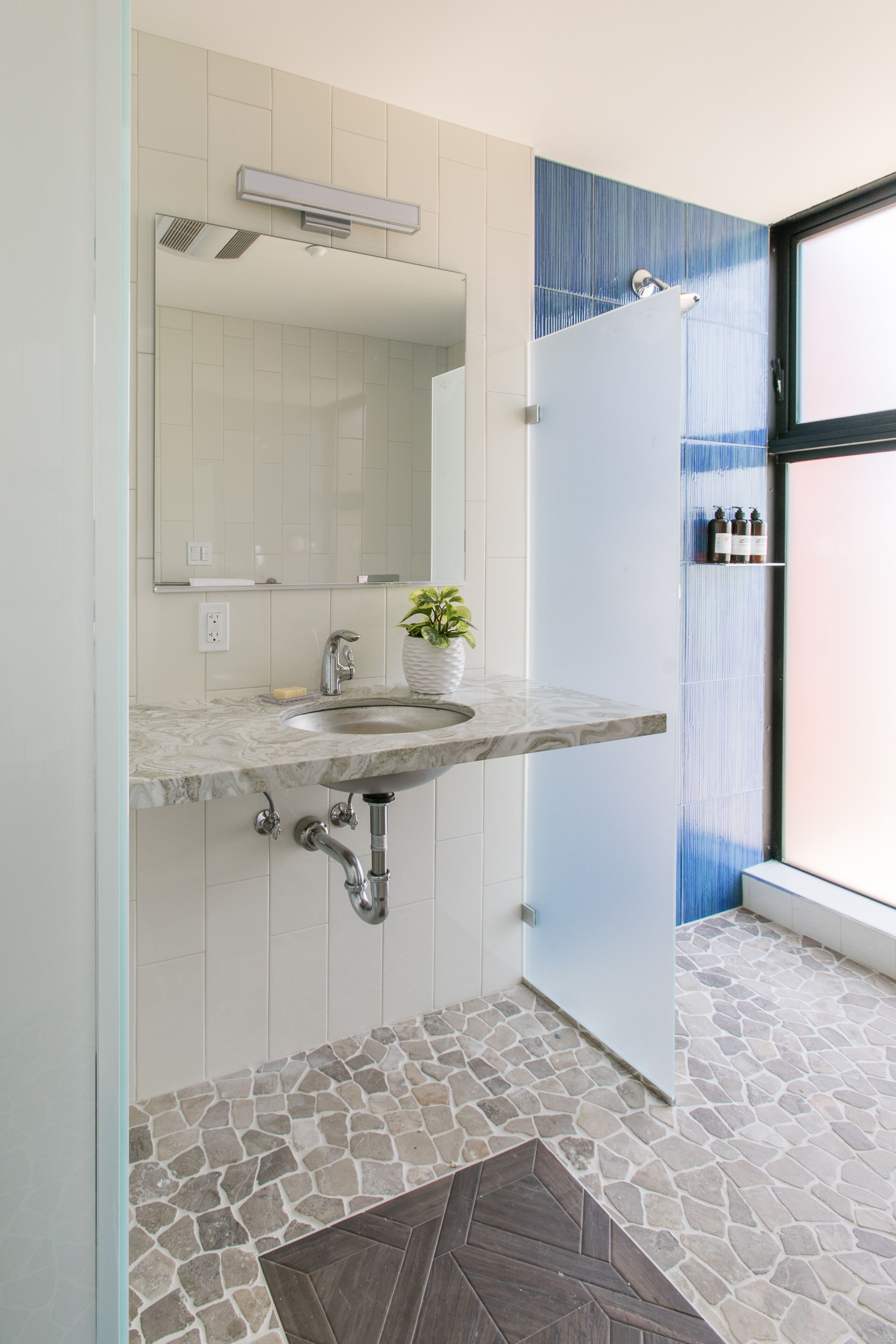 A bathroom with a marble sink, a mirror, a potted plant, and a shower area.