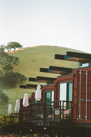 A building with a balcony, white umbrellas, and a view of a hill. - Geneseo Inn (Paso Robles)