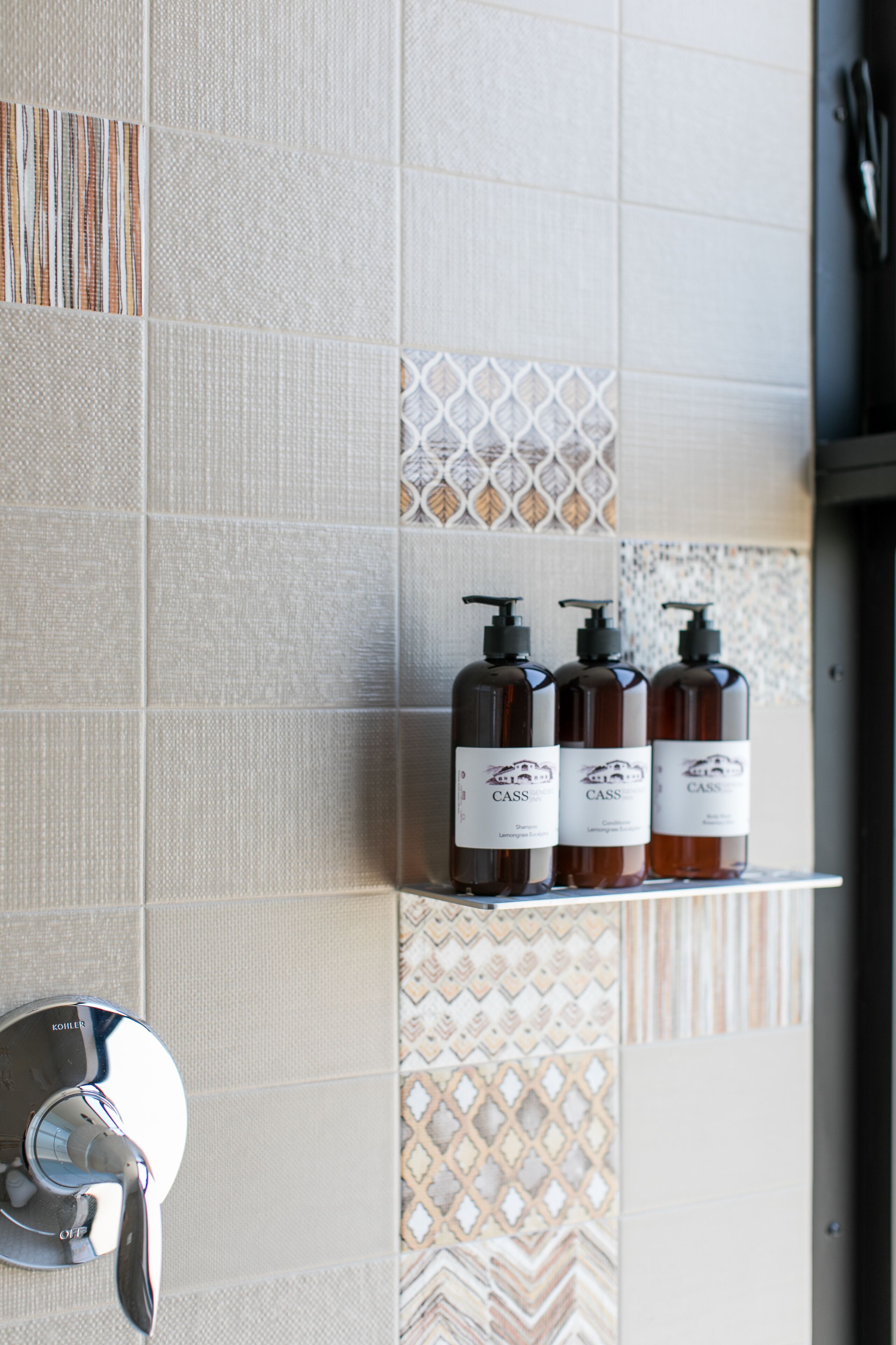 Une salle de bain avec une douche, un porte-serviettes et trois bouteilles de gel douche sur une étagère.