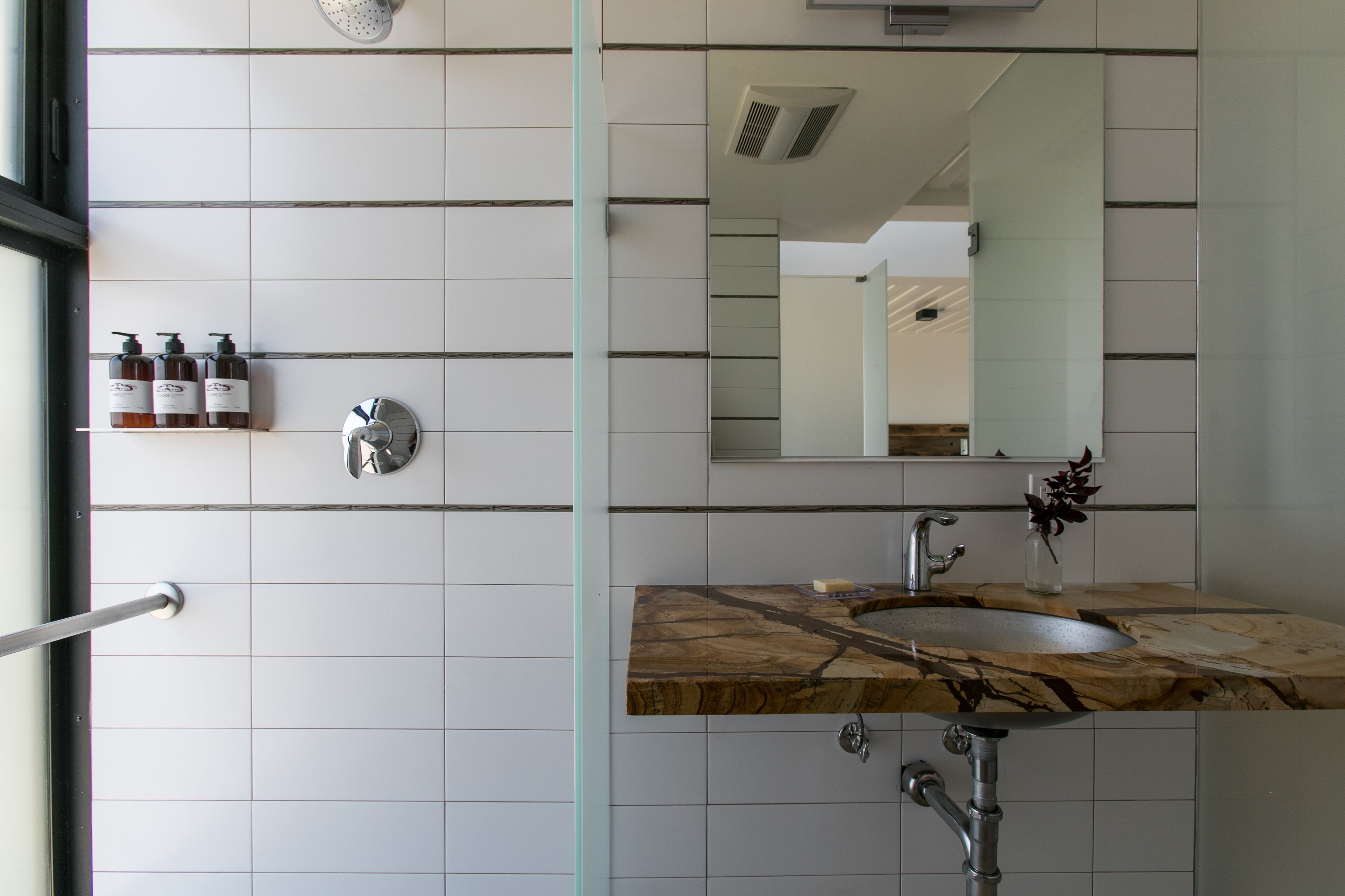 A bathroom with a marble sink, a mirror, and a showerhead.