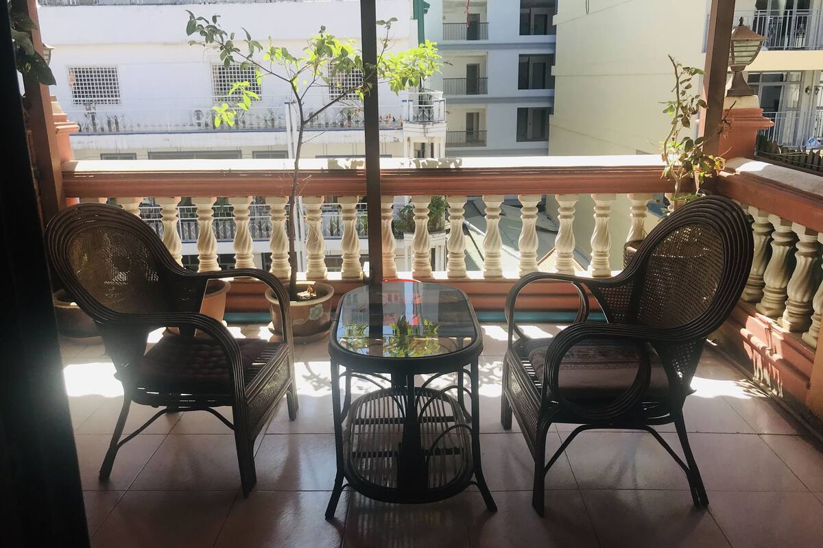Ein Balkon mit zwei Korbstühlen, einem kleinen Tisch und Topfpflanzen.