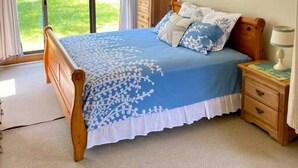 Ein Schlafzimmer mit einem großen Bett, einem Holzkopfende und Blick durch eine Glastür in einen Garten.