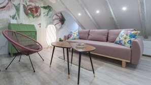 Une chambre à coucher confortable, aménagée en mezzanine, avec un plafond en pente, un canapé rose, un fauteuil vert et une petite table.