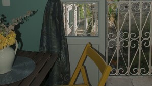 Une pièce donnant sur un mur de pierre et des bâtiments historiques, une fenêtre avec un rideau et une table en bois sur laquelle est posé un vase de fleurs.