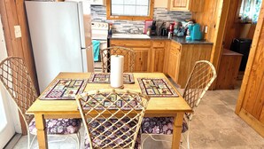 A wooden dining table with four chairs, a white wall-mounted microwave, a stove, and a window with blinds. - Waterfront Cabin #1, Onalaska, Lake Livingston, Texas (Onalaska)