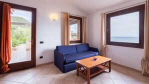 Una stanza con un divano blu, un tavolo in legno e vista mare attraverso un'ampia finestra.