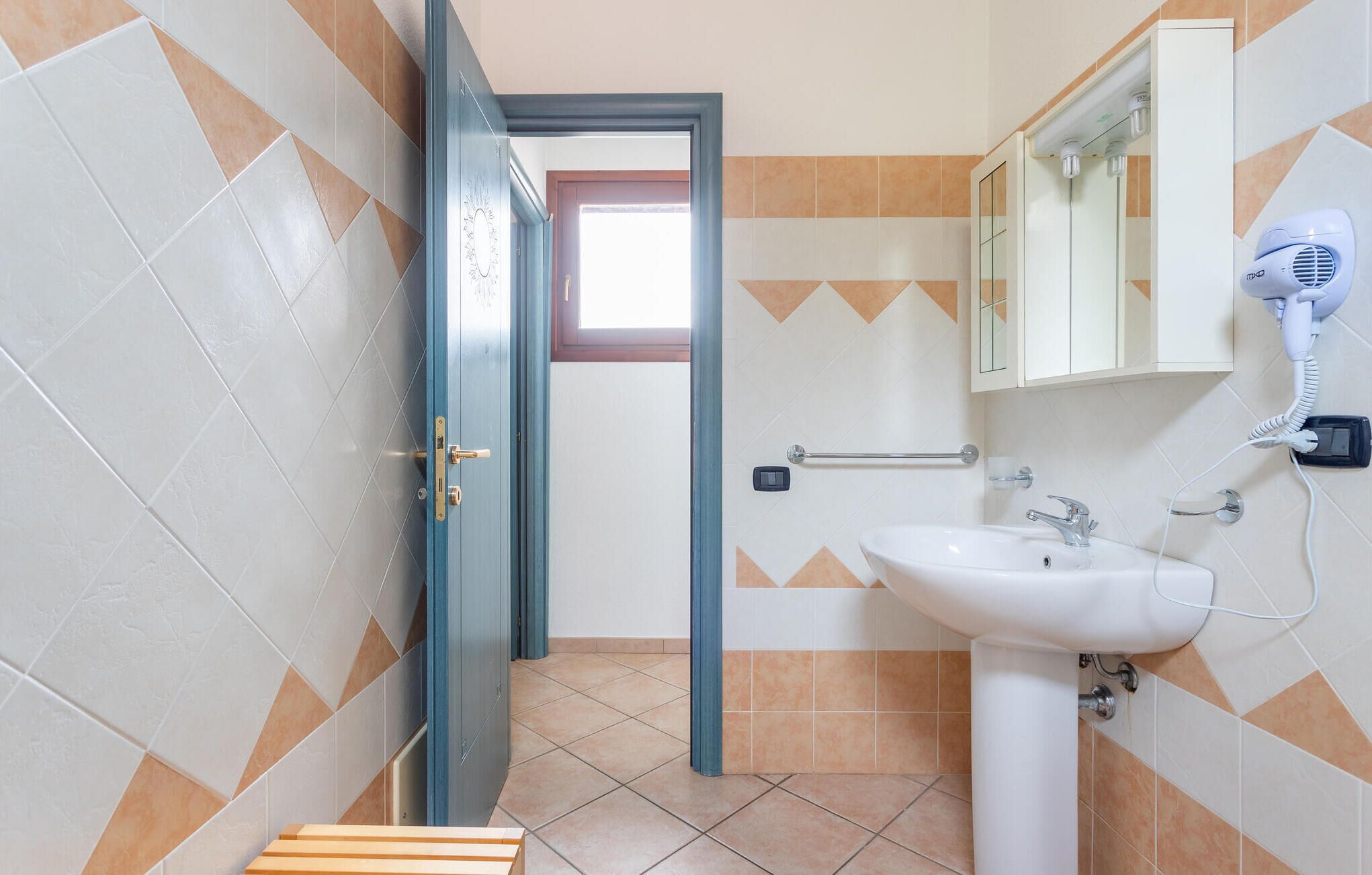 Ein Badezimmer mit einem weißen Waschbecken, einem Spiegel und einem Föhn an der Wand.