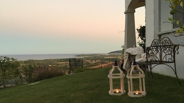 A grassy outdoor area with two lanterns and a metal bench, overlooking a distant landscape.