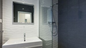 Un bagno moderno con un lavandino bianco, cabina doccia in vetro e specchio sopra il lavandino.