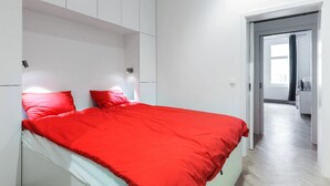 Camera da letto moderna con un letto grande, pareti bianche e un corridoio luminoso che porta al bagno.