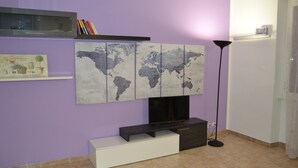 Quarto com parede roxa, obra de arte com mapa-múndi, televisão, estante de livros e abajur.
