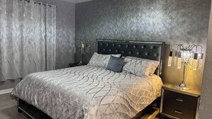 A bedroom with a tufted headboard, a bed with patterned bedding, a nightstand with a lamp, and a wall-mounted light fixture.