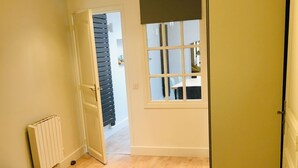 A bedroom with a bed, a radiator, a window with blinds, and a door leading to another room.