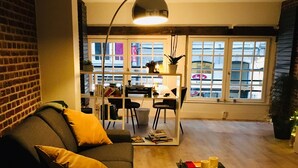 A modern living room with a dark-colored sofa, a coffee table, and a floor lamp. There is a dining area with a table and chairs in the background.