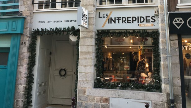 A storefront with a sign reading "LES INTREPIDES" and a door with a wreath.