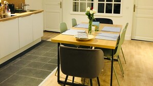 A modern kitchen with white cabinets, a wooden countertop, and a built-in oven. There is a dining area with a wooden table, chairs, and a vase with flowers.