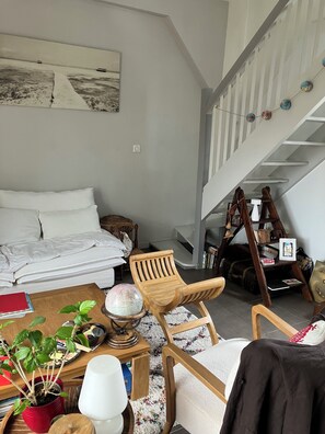 A living room with a sofa, a wooden chair, a coffee table with a globe, a red potted plant, and a staircase.
