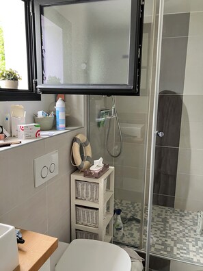 A bathroom with a shower, a toilet, a sink, a mirror, and a window.