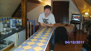 A man seated at a kitchen counter with a tiled backsplash, a coffee maker, and a television on a stand.