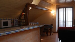 A kitchen with a microwave, coffee maker, and a checkered countertop. There is a dining area with a table and chairs, and a bed in the corner.
