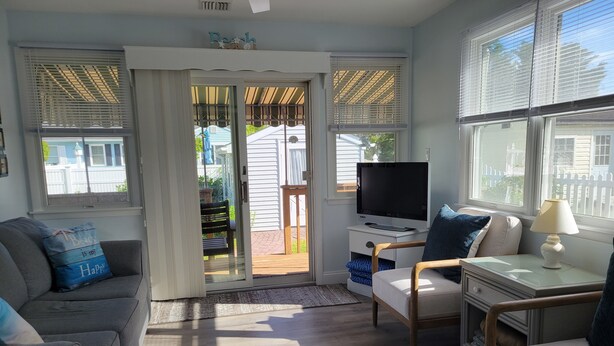 A living room with a grey sofa, a white armchair, a TV on a stand, and a small table with a lamp. - Relaxing Getaway on the Island.  (Cape May)