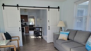 A living room with a grey sofa, wooden chairs, and a dining table. There is a kitchen in the background with cabinets and a stove. - Relaxing Getaway on the Island.  (Cape May)