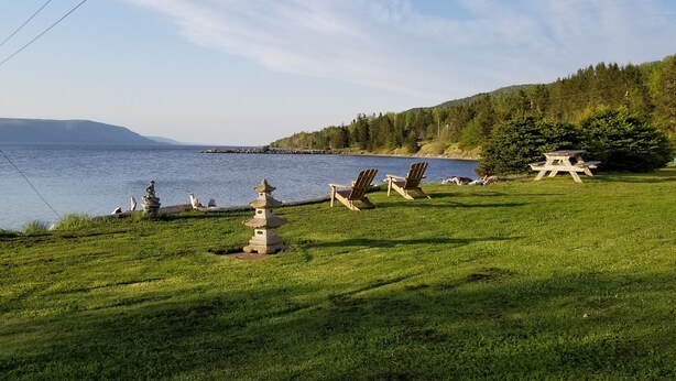 Zona arbolada con mesas de picnic y faroles de piedra junto a un lago, rodeada de árboles y colinas.